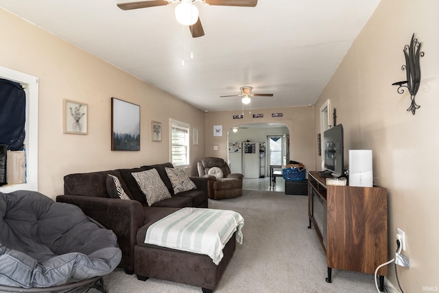living room featuring ceiling fan, light carpet, arched walkways, and plenty of natural light