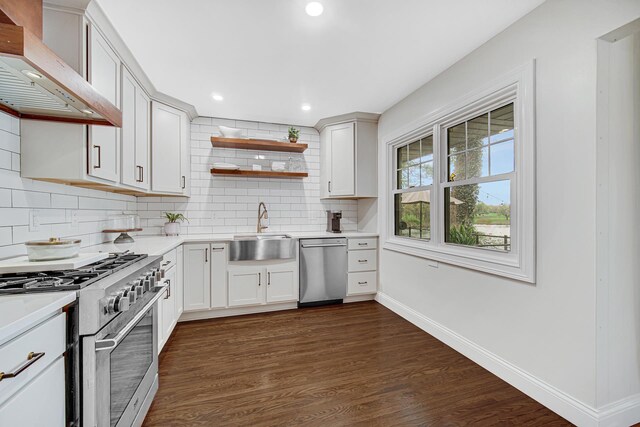 kitchen featuring stainless steel appliances, a sink, wall chimney range hood, tasteful backsplash, and light countertops