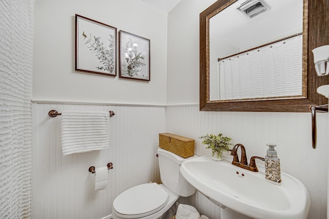 bathroom with a sink, wainscoting, toilet, and a shower with curtain