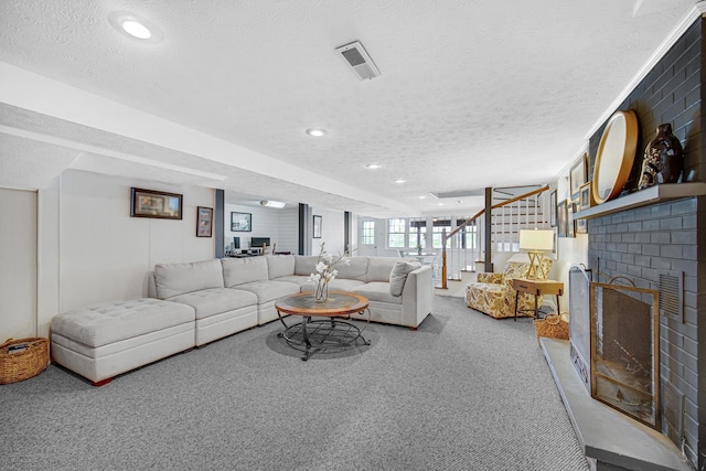 carpeted living area featuring a textured ceiling, stairway, a brick fireplace, and recessed lighting