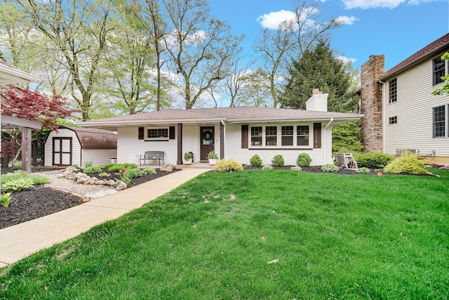 view of front of house featuring a storage shed, an outbuilding, a front yard, a chimney, and brick siding