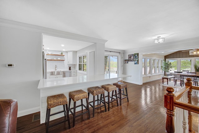 kitchen with light countertops, dishwasher, a breakfast bar, baseboards, and white cabinets