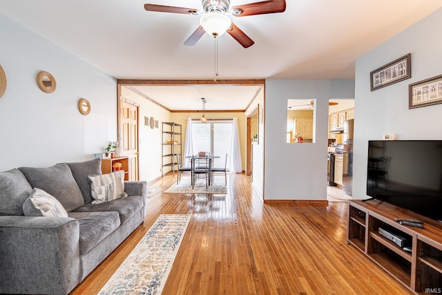 living area featuring a ceiling fan, light wood finished floors, and baseboards