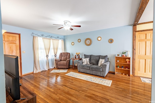living area featuring a ceiling fan, hardwood / wood-style flooring, and baseboards