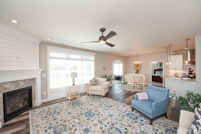 living room with dark wood finished floors, arched walkways, a tiled fireplace, a ceiling fan, and recessed lighting