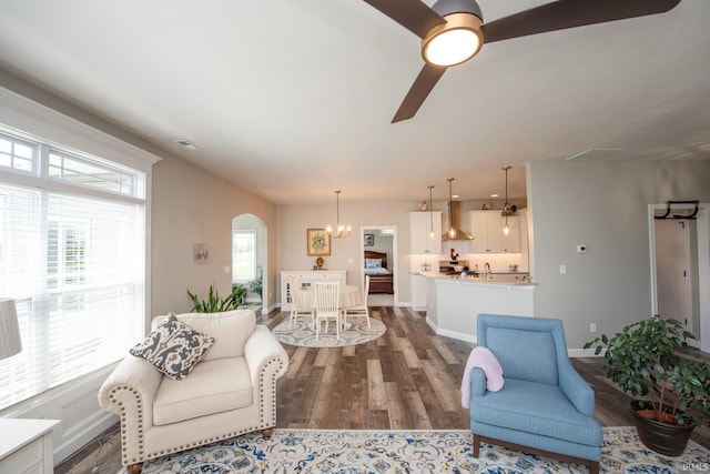 living room featuring a ceiling fan, arched walkways, wood finished floors, and a chandelier