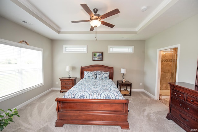 bedroom with a tray ceiling, light carpet, crown molding, baseboards, and ensuite bath