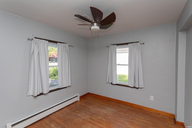 empty room featuring a baseboard heating unit, wood finished floors, a ceiling fan, and baseboards