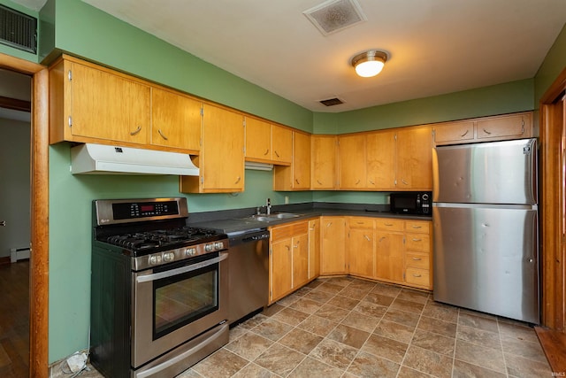 kitchen with stainless steel appliances, under cabinet range hood, a baseboard heating unit, dark countertops, and stone finish flooring