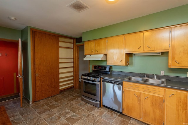 kitchen featuring stainless steel appliances, a sink, under cabinet range hood, dark countertops, and stone finish floors