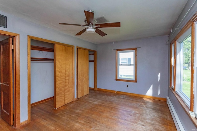 unfurnished bedroom featuring a baseboard radiator, multiple windows, wood finished floors, and multiple closets