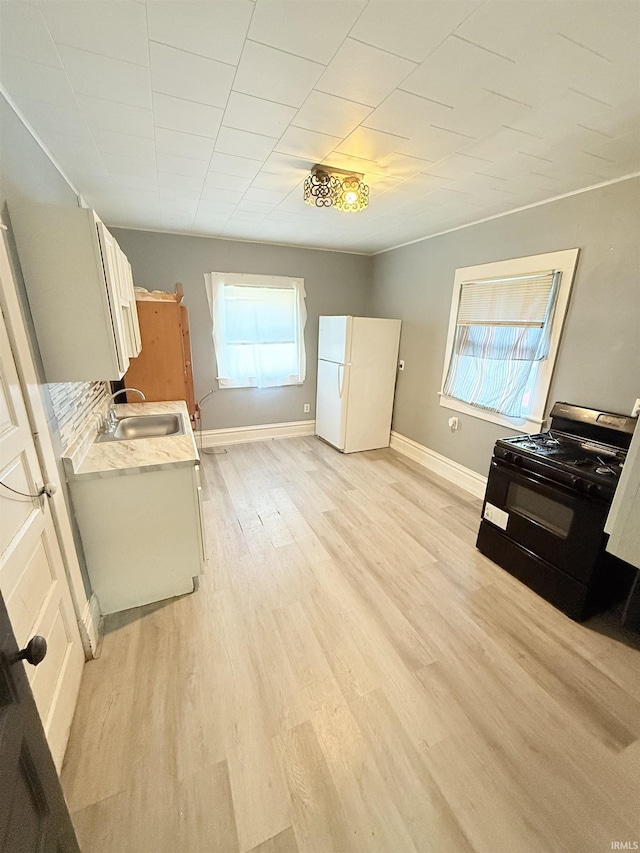 118 13th St, Logansport, IN 46947 - kitchen with black gas stove, freestanding refrigerator, a sink, light countertops, and light wood finished floors