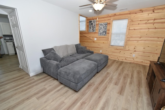 living room featuring a ceiling fan, light wood-style floors, and wood walls