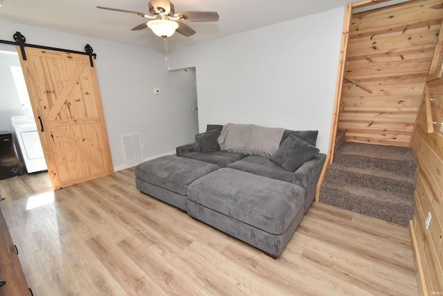 living room featuring washer / dryer, ceiling fan, wood finished floors, a barn door, and baseboards