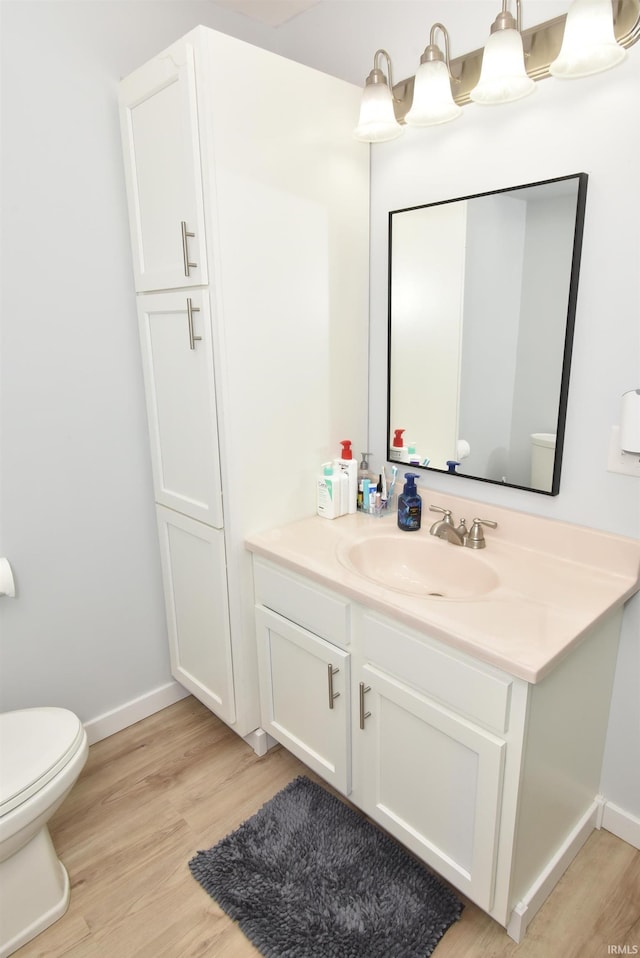 half bath with wood finished floors, vanity, baseboards, and toilet