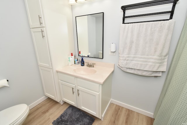 bathroom with wood finished floors, baseboards, vanity, and toilet