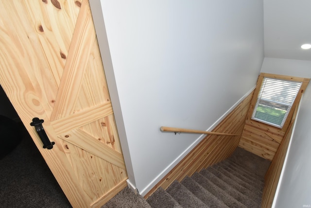 stairs with carpet, wooden walls, and wainscoting