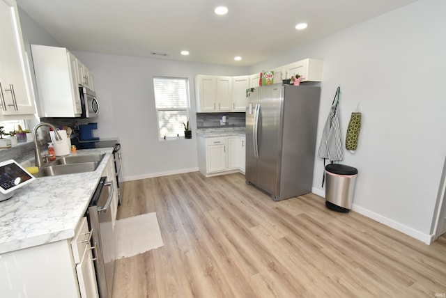 kitchen featuring appliances with stainless steel finishes, a sink, light wood finished floors, tasteful backsplash, and light countertops