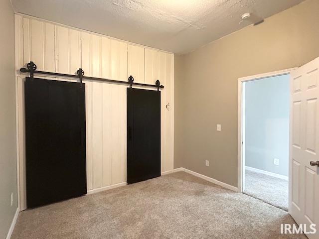 1023 W Franklin St, Evansville, IN 47710 - unfurnished bedroom with light colored carpet, a barn door, baseboards, and a textured ceiling