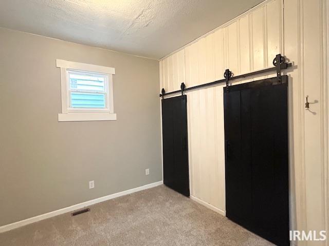 1023 W Franklin St, Evansville, IN 47710 - unfurnished bedroom with light carpet, a barn door, baseboards, and a textured ceiling