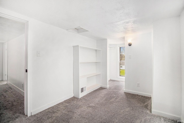 carpeted empty room with baseboards, a textured ceiling, and built in shelves