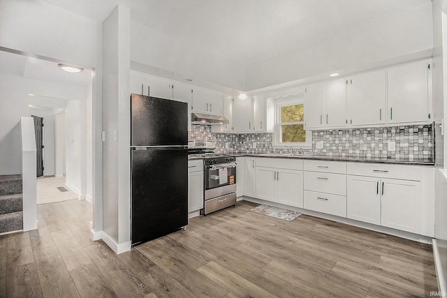 kitchen featuring freestanding refrigerator, gas stove, under cabinet range hood, light wood finished floors, and dark countertops