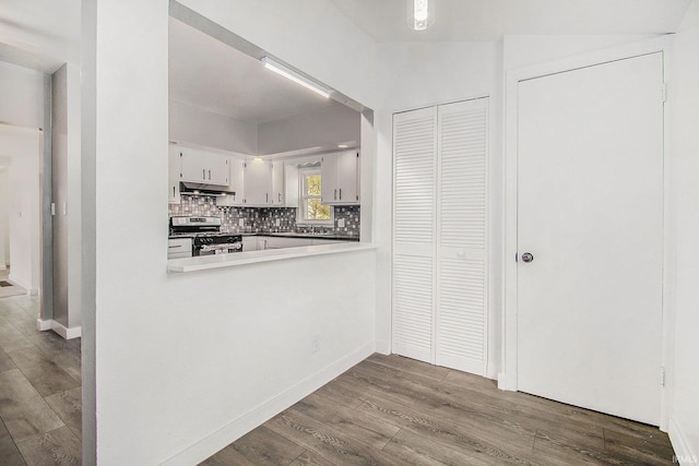 kitchen with stainless steel gas range oven, under cabinet range hood, wood finished floors, backsplash, and white cabinets