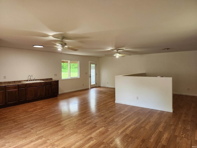 unfurnished living room with a sink, ceiling fan, light wood-style flooring, and baseboards