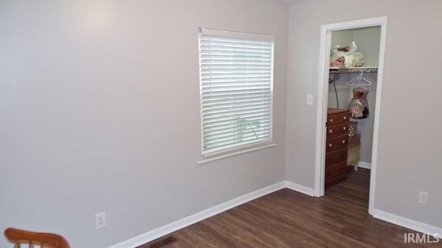 unfurnished bedroom with a spacious closet, baseboards, dark wood-style floors, and a closet