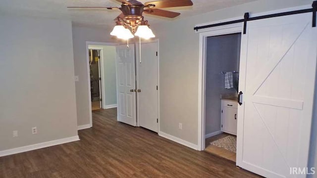 unfurnished room featuring a barn door, wood finished floors, ceiling fan, and baseboards