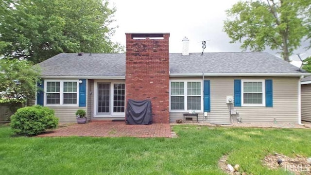 rear view of house with a chimney, a yard, a patio, and a shingled roof