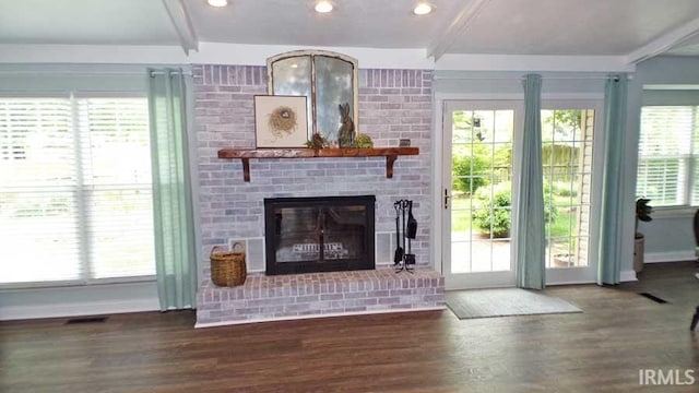 unfurnished living room featuring beamed ceiling, healthy amount of natural light, wood finished floors, a brick fireplace, and baseboards