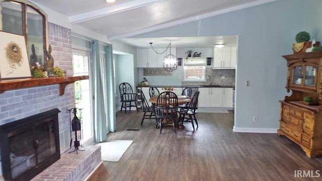 dining space featuring dark wood finished floors, a brick fireplace, lofted ceiling, a chandelier, and baseboards