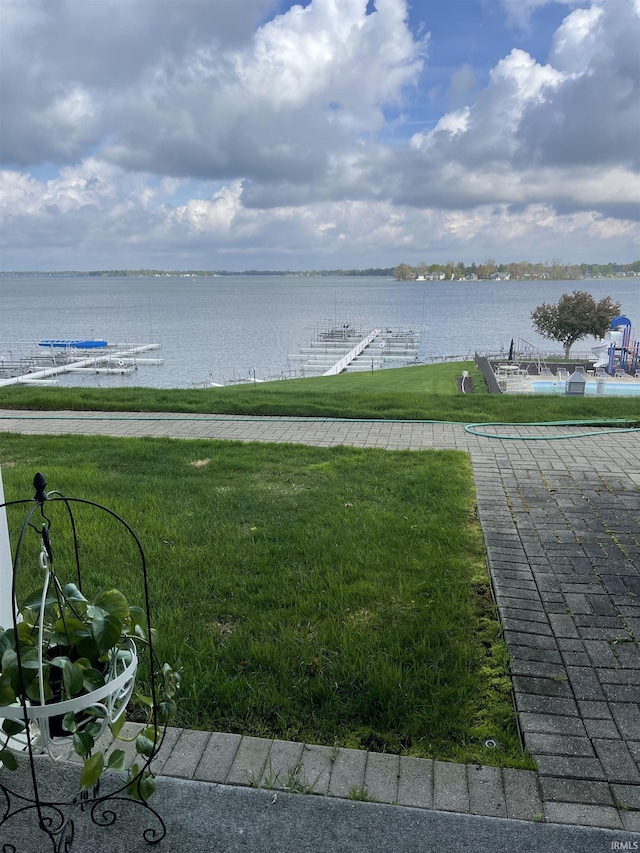 view of green lawn with a water view and a dock