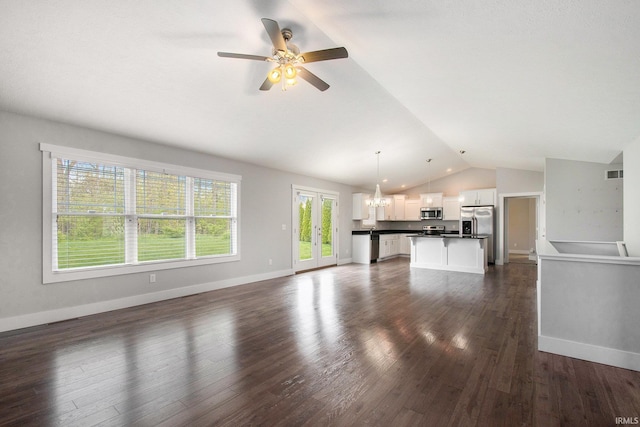 unfurnished living room featuring vaulted ceiling, ceiling fan, a chandelier, dark wood finished floors, and baseboards