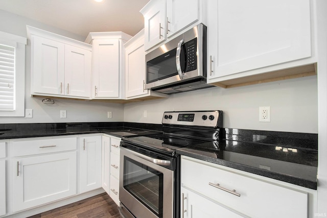 kitchen with appliances with stainless steel finishes, white cabinets, dark wood-type flooring, and dark stone countertops