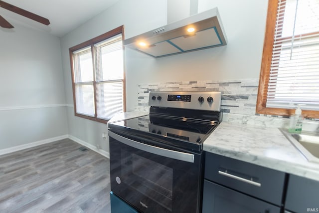kitchen featuring stainless steel range with electric stovetop, tasteful backsplash, wall chimney exhaust hood, a ceiling fan, and wood finished floors