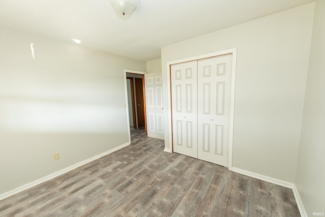 unfurnished bedroom with wood finished floors, baseboards, and a closet