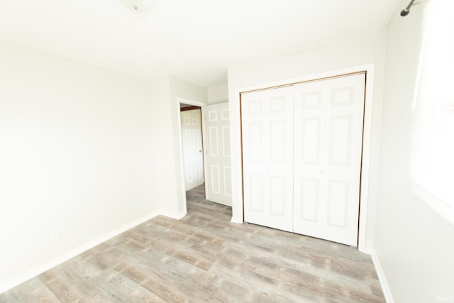unfurnished bedroom featuring light wood-style floors, baseboards, and a closet