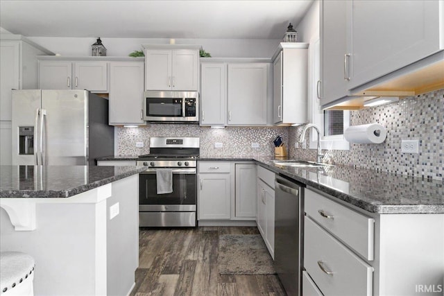 kitchen featuring stainless steel appliances, a sink, dark wood-style flooring, tasteful backsplash, and dark stone countertops