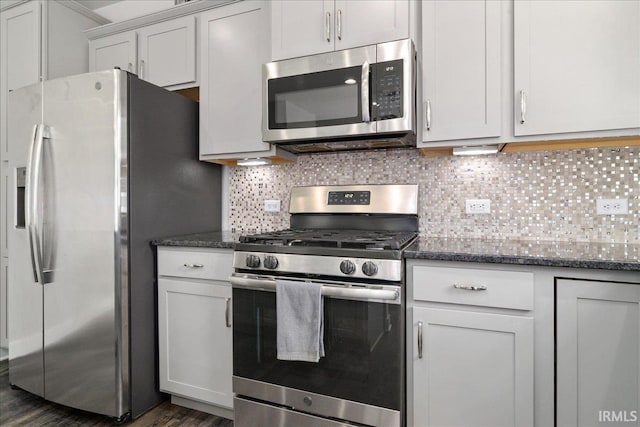 kitchen with appliances with stainless steel finishes, backsplash, dark wood finished floors, and dark stone countertops