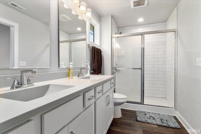 bathroom with a shower stall, wood finished floors, toilet, double vanity, and recessed lighting