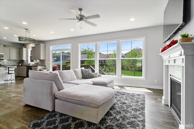 living area featuring recessed lighting, ceiling fan, baseboards, a glass covered fireplace, and dark wood finished floors