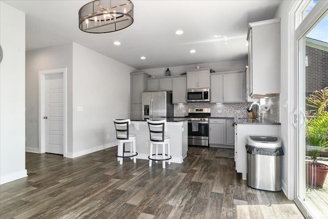 kitchen featuring stainless steel appliances, a center island, tasteful backsplash, dark wood finished floors, and a kitchen breakfast bar