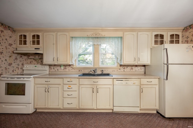 kitchen featuring cream cabinets, white appliances, a sink, wallpapered walls, and carpet