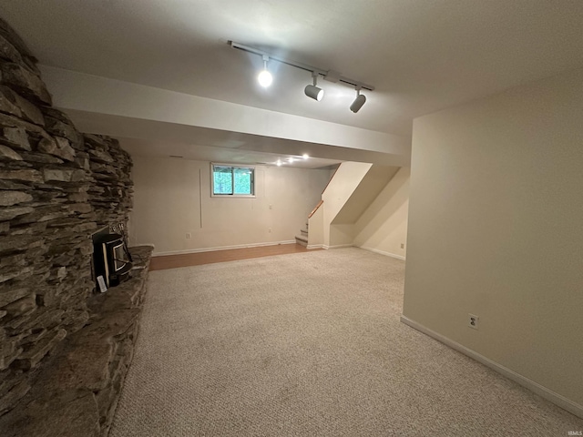 below grade area featuring light colored carpet, stairs, track lighting, and baseboards