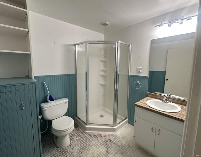 bathroom with a wainscoted wall, a shower stall, vanity, tile patterned flooring, and toilet