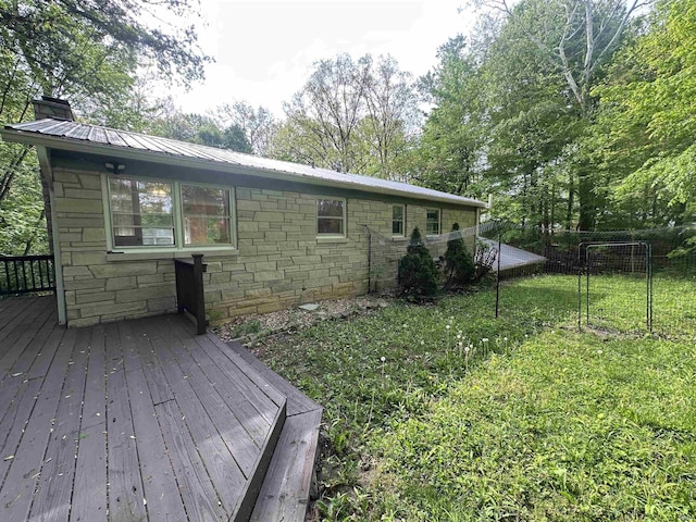 rear view of property featuring a deck, a chimney, stone siding, and metal roof