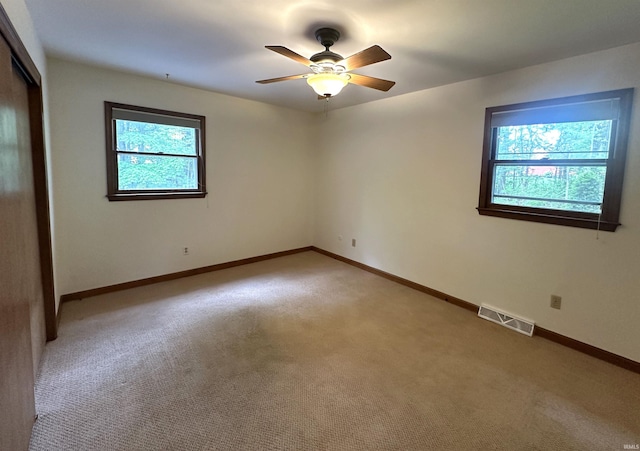 empty room with light carpet, a ceiling fan, and baseboards