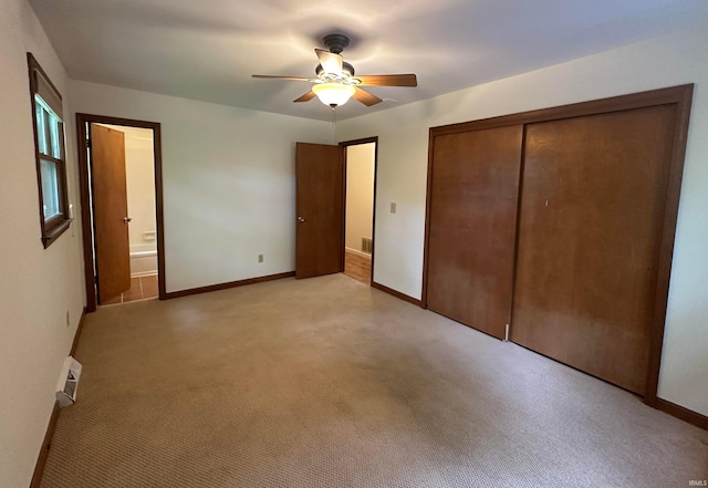 unfurnished bedroom featuring a closet, ceiling fan, light carpet, baseboards, and ensuite bathroom